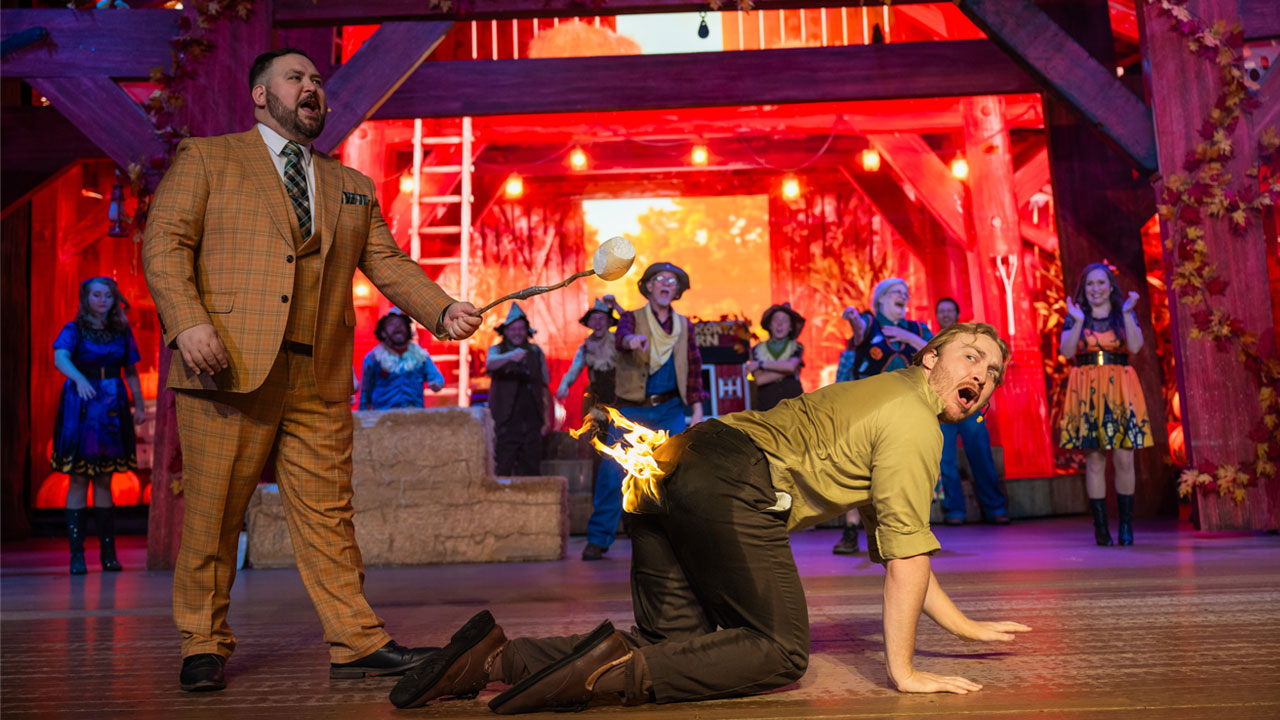 A man roasting a marshmallow over a fire on the rear end of another guy who looks distressed