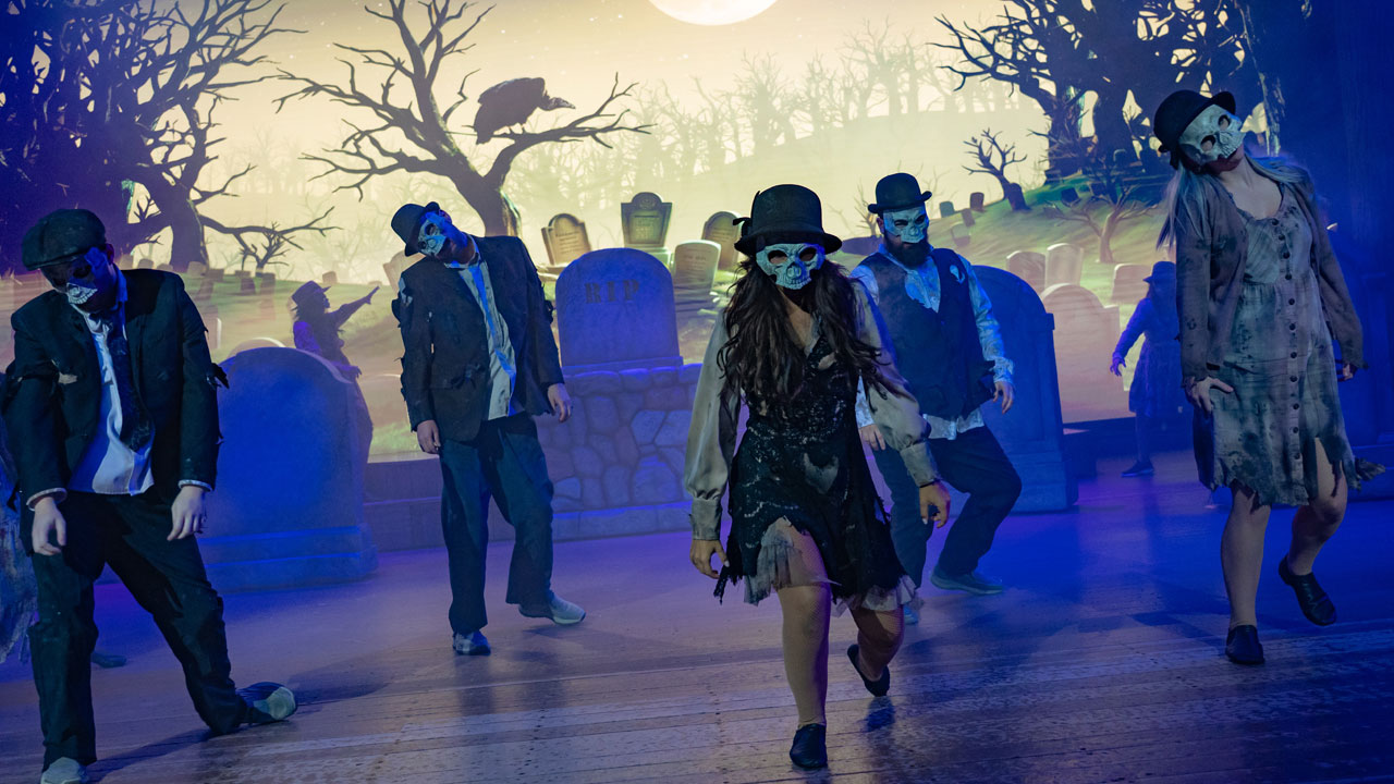 A group of shambling zombies walk through a graveyard