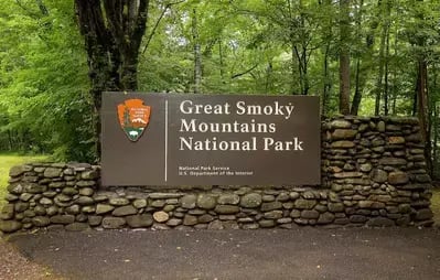 Sign for Great Smoky Mountains National Park in Tennessee with stone wall and forest in the background