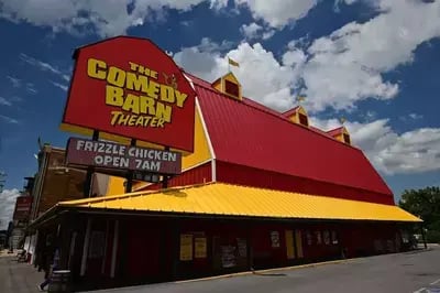 Front view of the Comedy Barn Theater in Pigeon Forge with yellow and red barn-style building and marquee sign.