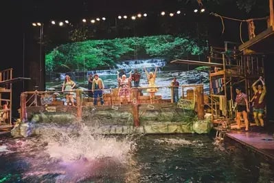 Stage set with swimming hole and waterfall at Hatfield & McCoy Dinner Feud, featuring props, performers and splashing water.